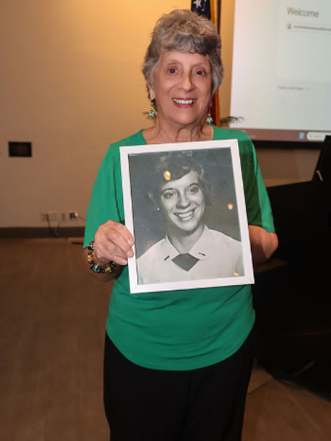 Woman in green holding a framed black-and-white portrait of a woman veteran, honoring her memory