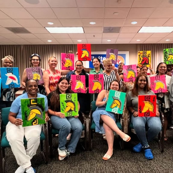 Group of women holding hand-painted canvases from an SDWVA paint night event