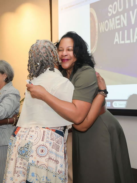 Two women sharing a warm embrace in front of the SDWVA presentation screen
